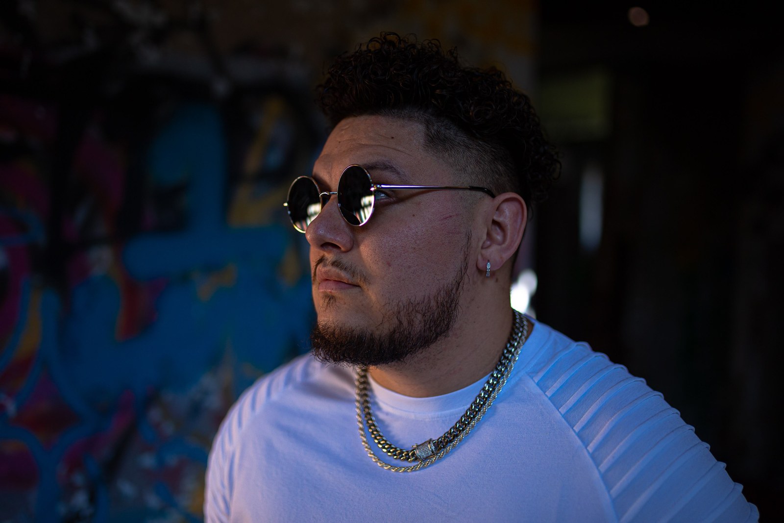 Aveek in sunglasses against a graffiti-covered wall